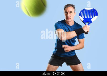 Porträt eines Mannes, der Paddeltennis spielt und einen Ball mit der Rückhand trifft. Er trägt blau-schwarze Sportkleidung und einen blau isolierten Hintergrund. Vorderansicht Stockfoto