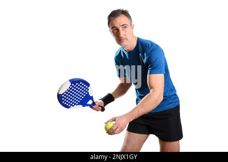 Porträt eines Mannes, der Padel in Servierposition spielt, mit Schläger und Ball in den Händen und blau-schwarzem Sportkostüm auf weißem, isoliertem Hintergrund. Front V Stockfoto