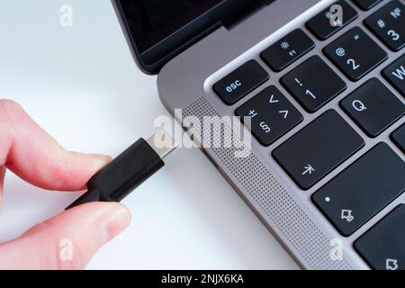 Nahaufnahme einer Hand, die ein USB-Typ-C-Kabel an einen isolierten Laptop anschließt. Modernes, bequemes Hafenkonzept. Stockfoto