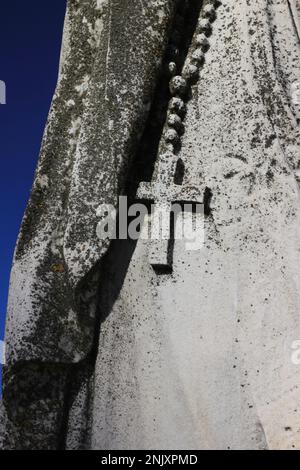 Ein christliches Kreuz, das an einer Statue hängt und in Naturstein geschnitzt ist. Stockfoto