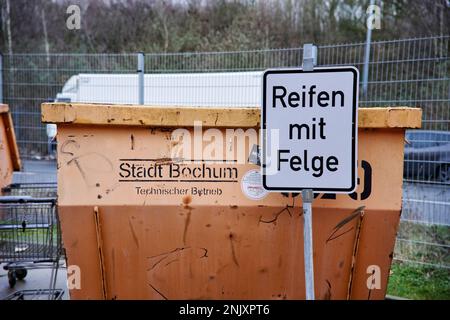 Orangene Müllcontainer mit Beschriftung für die Müllart die abgegeben werden darf. Reifen mit Felge. Stockfoto