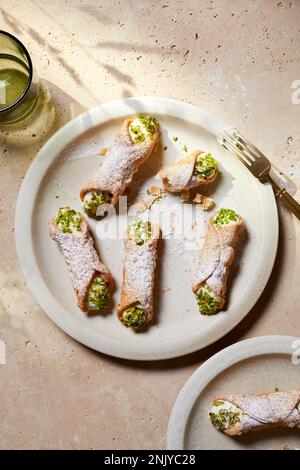 Blick von oben auf köstliches italienisches Cannoli-Dessert mit Frischkäse und Pistaziennüssen auf weißem Teller mit Gabel Stockfoto