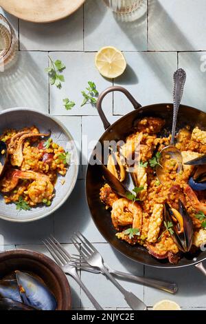 Blick von oben auf die schmackhafte Paella mit Meeresfrüchten, serviert auf einem Teller und auf weißen Fliesen Stockfoto