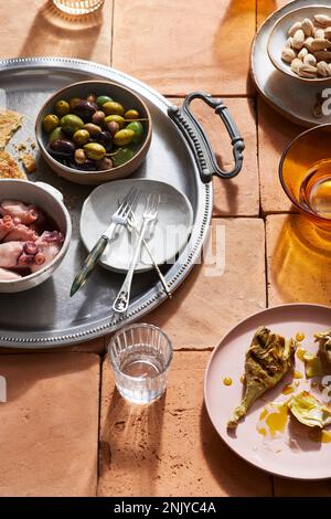 Verschiedene spanische Mezze-Gerichte mit Oliven, Huhn und Nüssen sowie Tintenfisch-Tentakeln, serviert auf Tellern mit Gabeln Stockfoto