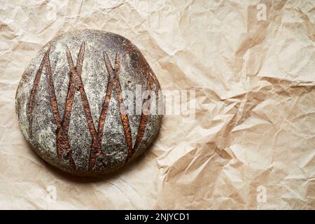 Blick von oben auf köstliches hausgemachtes rundes Sauerteigbrot mit knuspriger Kruste auf Pergamentpapier Stockfoto