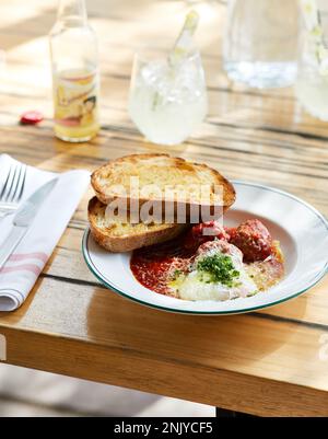 Leckere Tomatensuppe mit Fleischbällchen, serviert auf einem Teller mit Brot und Kräutern im Restaurant Stockfoto
