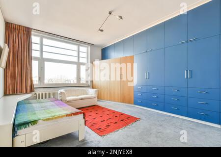 Innendesign des geräumigen Schlafzimmers mit Teppichboden und rotem Teppich in der Nähe des Einzelbetts Stockfoto