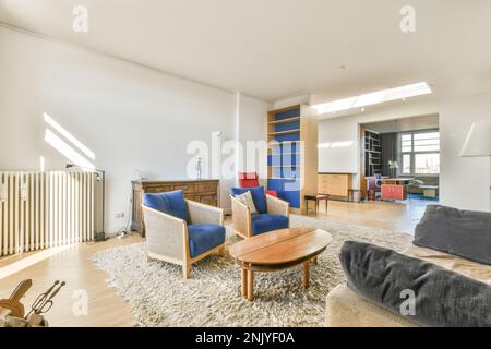 Helle Lounge mit beigefarbenem Sofa an der weißen Wand und Holzsesseln in der Nähe des Couchtisches auf Teppich Stockfoto