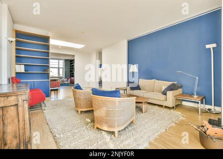 Helle Lounge mit beigefarbenem Sofa an blauer Wand und Holzsesseln in der Nähe des Couchtisches auf Teppich Stockfoto