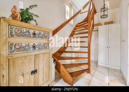 Innenseite des hellen Korridors mit weißem Kleiderschrank und antiken Schubladen in der Nähe der hölzernen Wendeltreppe Stockfoto