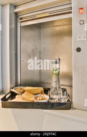 Wanderung mit leckeren Käsekuchen auf dem Schneidebrett und kleinen Schüsseln mit Nüssen in der Nähe einer Flasche Mojito und Gläsern in der Nähe des Aufzugs Stockfoto