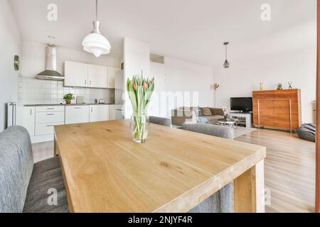 Das moderne, offen gestaltete Apartment verfügt über Küche und Essbereich vor dem Wohnzimmer, das mit Tulpen in Vase dekoriert ist Stockfoto
