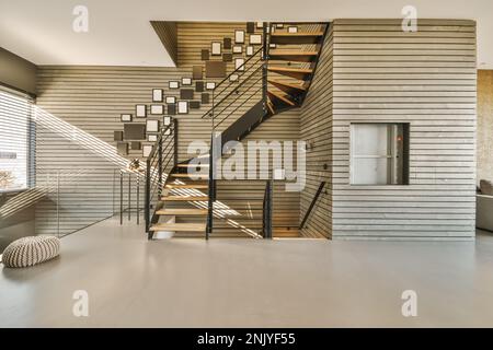 Innendesign eines modernen Hauses mit Holz- und Metalltreppen, dekoriert mit Fotorahmen nahe Glaszaun und Wollfußhocker Stockfoto