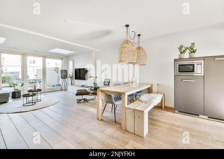 Innendesign der modernen Küche mit Schränken und eingebauter Mikrowelle in der Nähe von Holztischstühlen und einer Bank an den Fenstern in l Stockfoto