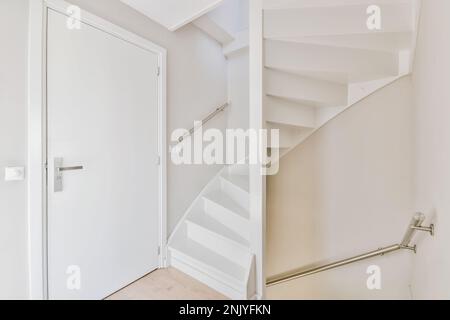 Innendesign des Flurs mit weißen Wänden und Treppen mit Metallklammer in der Nähe der Tür mit beigefarbenem Boden in zeitgenössischem Haus Stockfoto