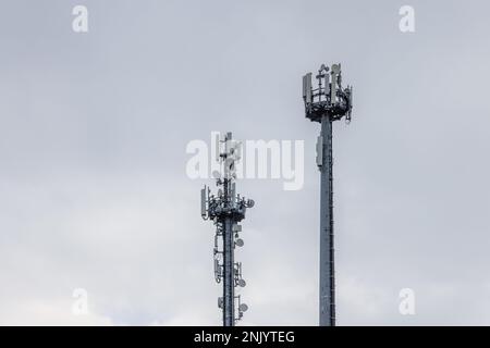 Zwei Mobilfunkmasten mit verschiedenen Antennen und Signalverstärkern gegen einen bewölkten Himmel Stockfoto