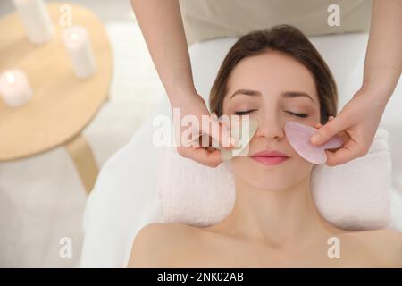 Junge Frau, die im Schönheitssalon eine Gesichtsmassage mit Gua-sha-Werkzeugen erhält Stockfoto