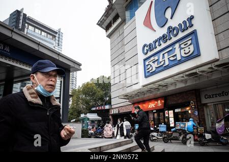 Die Leute gehen an einem riesigen Schild von Carrefour Store in Wuhan vorbei. Carrefour trat im Jahr 1995 in den chinesischen Markt ein und expandierte sehr schnell, um einen großen Marktanteil zu sichern. Die Einnahmen nahmen jedoch mit zunehmender Konkurrenz ab. Im Jahr 2019 verkaufte der französische Einzelhändler rund 80 % seines „verlustbringenden“ Geschäftsbereichs in China für 4,8 Mrd. CNY an das in Jiangsu ansässige Unternehmen „Suning“, was zu diesem Zeitpunkt 699 Mio. USD entsprach. In diesem Monat haben Berichte über Engpässe in den zahlreichen lokalen Carrefour-Filialen die Aufmerksamkeit der Kunden erregt. Mehrere Leute begannen sich zu beschweren, dass sie es waren Stockfoto