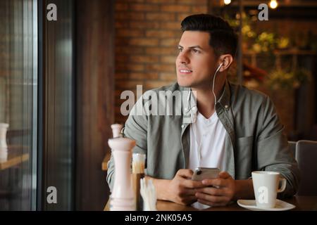 Mann mit Smartphone, der Hörbuch am Tisch im Café hört Stockfoto