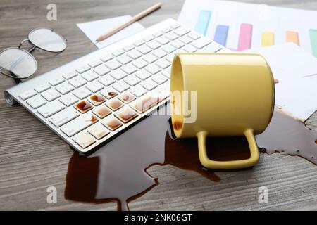 Eine Tasse Kaffee wurde über die Computertastatur auf dem hölzernen Büroschreibtisch verschüttet Stockfoto