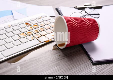 Eine Tasse Kaffee wurde über die Computertastatur auf dem hölzernen Büroschreibtisch verschüttet Stockfoto