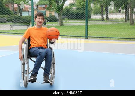 Behinderter Teenager im Rollstuhl mit Basketballball im Freien Stockfoto