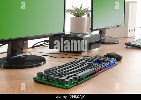 Moderner Computer und RGB-Tastatur auf Holztisch im Innenbereich Stockfoto