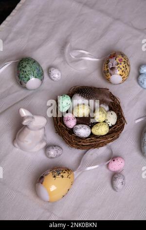 Foto auf einer weißen Tischdecke mit vielen dekorativen Eiern und einem weißen Osterei und einem Nest Wachteleier auf dem Tisch Stockfoto