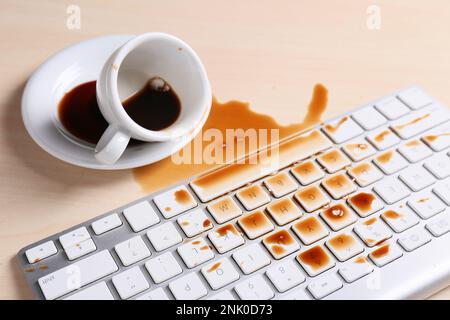 Eine Tasse Kaffee wurde über die Computertastatur auf dem Holztisch verschüttet Stockfoto