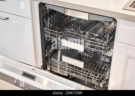 Leere eingebaute Geschirrspüler mit geöffneter Tür. Haushaltsgerät Geschirrspülmaschine in moderner Küche. Weiße Farbtöne und saubere Küche. Stockfoto