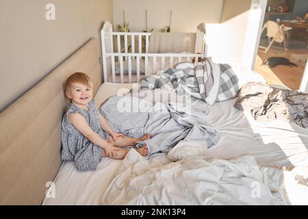 Hausreinigung. Ein glückliches kleines Mädchen, die Helferin hat Spaß und lächelt, während sie in einer hellen Wohnung ist. Hilft Eltern, die Bettwäsche zu wechseln Stockfoto