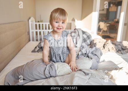 Hausreinigung. Ein glückliches kleines Mädchen, die Helferin hat Spaß und lächelt, während sie in einer hellen Wohnung ist. Hilft Eltern, die Bettwäsche zu wechseln Stockfoto