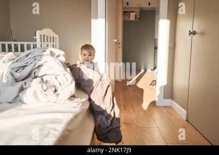 Hausreinigung. Ein glückliches kleines Mädchen, die Helferin hat Spaß und lächelt, während sie in einer hellen Wohnung ist. Hilft Eltern, die Bettwäsche zu wechseln Stockfoto