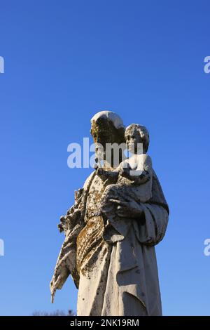 Eine getragene und verwitterte Natursteinstatue des Heiligen Joseph, die das Jesuskind in seinen Händen trägt. Stockfoto