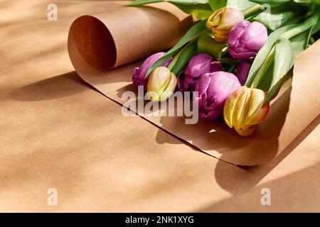 Farbenfrohe Tulpen auf handgemachtem Papier. Gelbe, rosafarbene, magentafarbene oder fuchsianische Tulpen auf braunem Geschenkpapier. Stummgeschalteter Ton. Frühlingsferien mit Blumendekor. Stockfoto