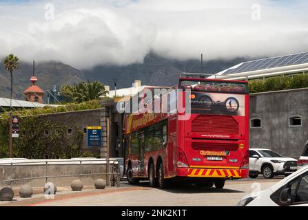 Kapstadt Südafrika. 2023. Ein roter Touristenbus mit offenem Oberdeck fährt links in eine belebte Straße. Stockfoto