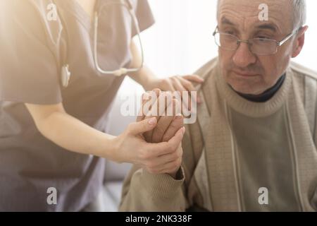Fürsorgliche Krankenschwester spricht mit altem Patienten hält seine Hand sitzen im Wohnzimmer bei Homecare Besuch bieten psychologische Unterstützung zuhören klagt Empathie zeigen Stockfoto