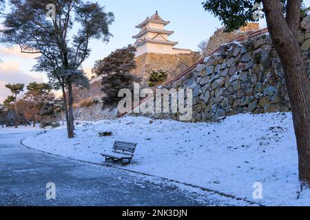 Die historische japanische Burg ragt über einer schneebedeckten Bank entlang des Parkwegs Stockfoto