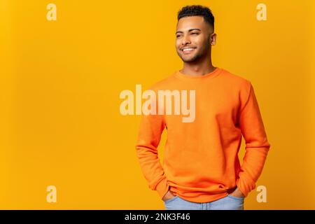 Der stilvolle, gutaussehende junge indische Mann hat gute Laune, genießt den sonnigen Tag und posiert isoliert auf gelbem Hintergrund Stockfoto