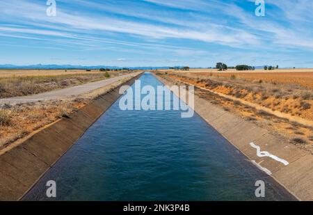 In der Ferne erstreckt sich ein langer, gerader Bewässerungskanal in Spanien, dessen klares blaues Wasser den hellen, sonnigen Himmel reflektiert Stockfoto