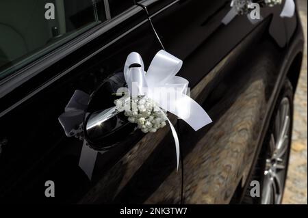 Dekorationen und Details auf dem Hochzeitsauto weißes Band und winzige Blumen am Türgriff eines schwarzen, modernen Autos kleine Feldtiefe Stockfoto