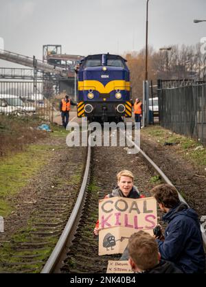Amsterdam, Niederlande, 22.02.2023, junger Klimaaktivist mit einem Schild mit der Aufschrift "Coal kills", der auf einer Bahnstrecke vor dem Kohlezug sitzt Stockfoto