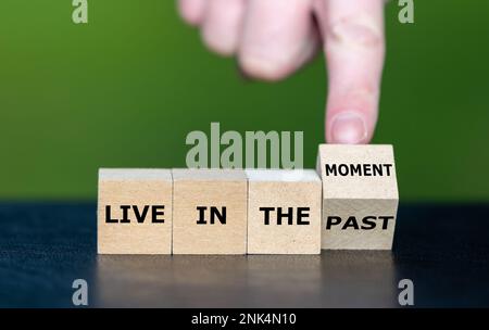 Die Hand dreht den Holzwürfel und ändert den Ausdruck „in der Vergangenheit leben“ in „im Moment leben“. Stockfoto