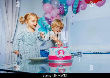 Ein Mädchen und ein Junge sitzen auf der Geburtstagsparty und zeigen auf Kuchen Stockfoto