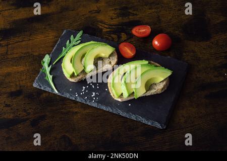 Sandwiches mit Avocado mit Gewürzen und Kirsche auf schwarzem Steinhintergrund, Draufsicht. Draufsicht. Platz für Text. Hochwertiges Foto Stockfoto