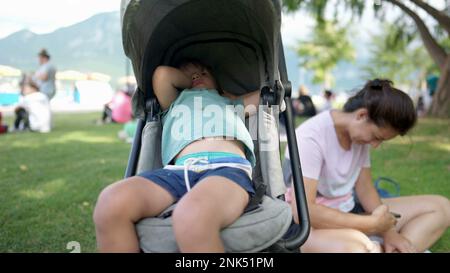 Ein schläfriger kleiner Junge, der im Kinderwagen sitzt und vom Nickerchen aufwacht. Das Kind wacht auf, nachdem es mit seiner Mutter während des Nachmittags draußen im Park geschlafen hat Stockfoto