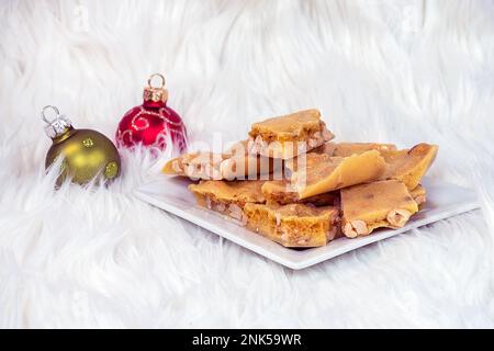 Weihnachtsschmuck in Fell mit Erdnussbrüchig auf weißem quadratischem Teller Stockfoto