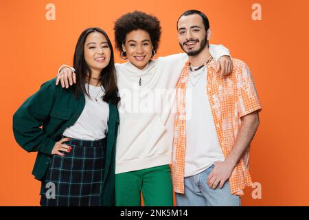 Fröhliche afroamerikanische Frau, die trendige, multirassische Freunde auf einem orangefarbenen Stock-Bild umarmt Stockfoto