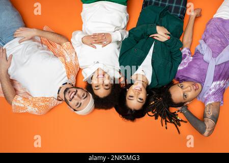Draufsicht auf fröhliche und stilvolle multikulturelle Freunde auf orangefarbenem Hintergrund, Stockbild Stockfoto