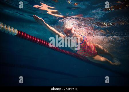 Dynamische Aufnahme eines professionellen weiblichen Schwimmertrainings im Innenpool. Entwicklungsgeschwindigkeit. Unterwasserblick. Sportbegriff, Ausdauer Stockfoto